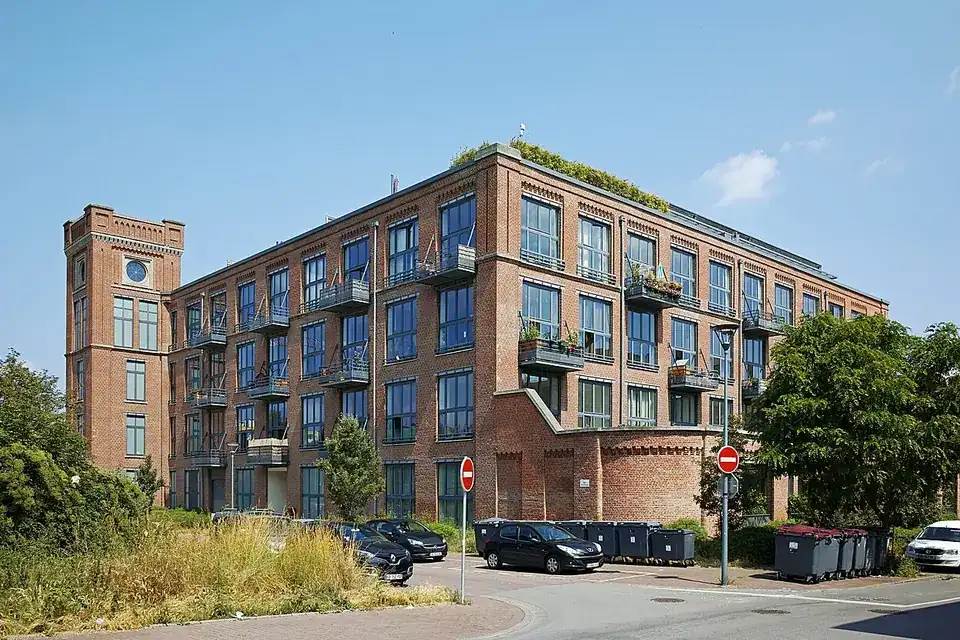 Ancien bâtiment industriel en brique transformé en logements, avec balcons et une tour